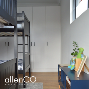 Childrens bedroom with two black bunk beds and a blue lowline cupboard with childrens books. There is a row of cupboard doors along the back wall