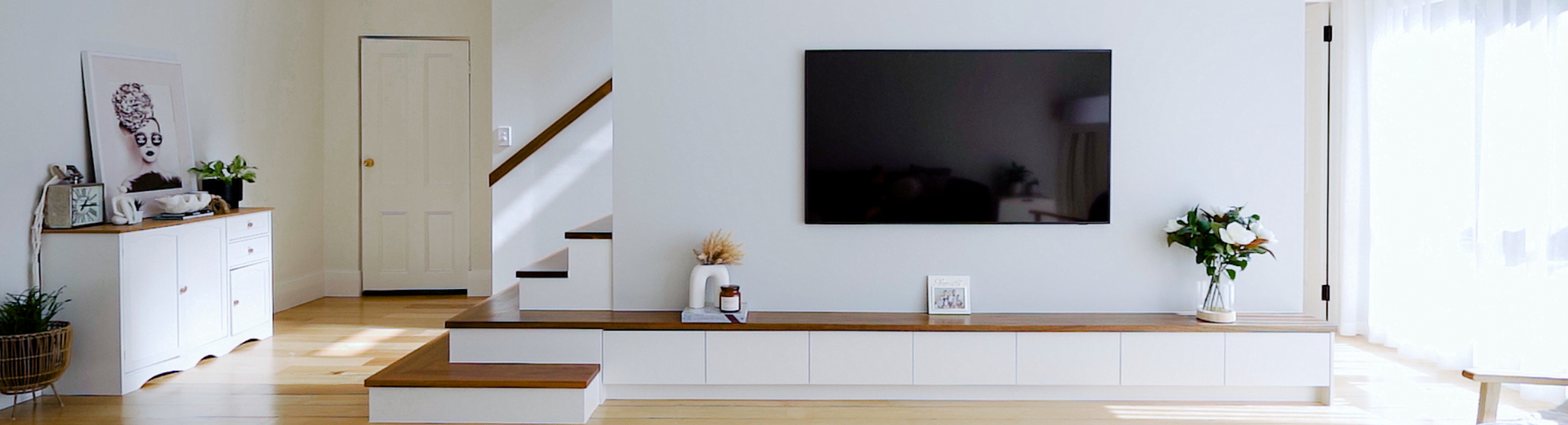 Open plan living room with large wall mounted TV and timber staircase.