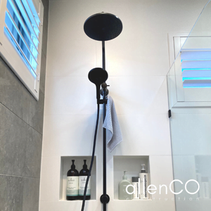 Mounted black shower head on a white tiled wall of an ensuite bathroom