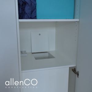 Close up of an open cupboard door showing the open lid of a laundry chute