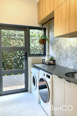 New renovated laundry with timber cupboards, tiled splashback and a glass door