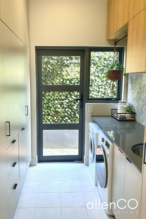 Newly renovated laundry with lots of cupboards and a glass door leading outside