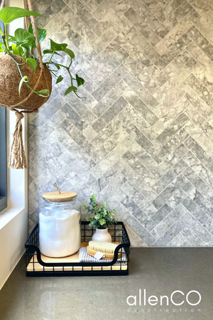 Close up of marble herringbone tile laundry splashback with hanging plant pot and a tray with laundry salts and scrubbing brush