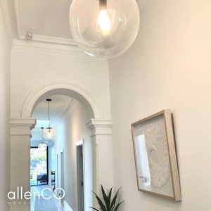 White hallway with a large round pendant light, artwork on the wall and an archway