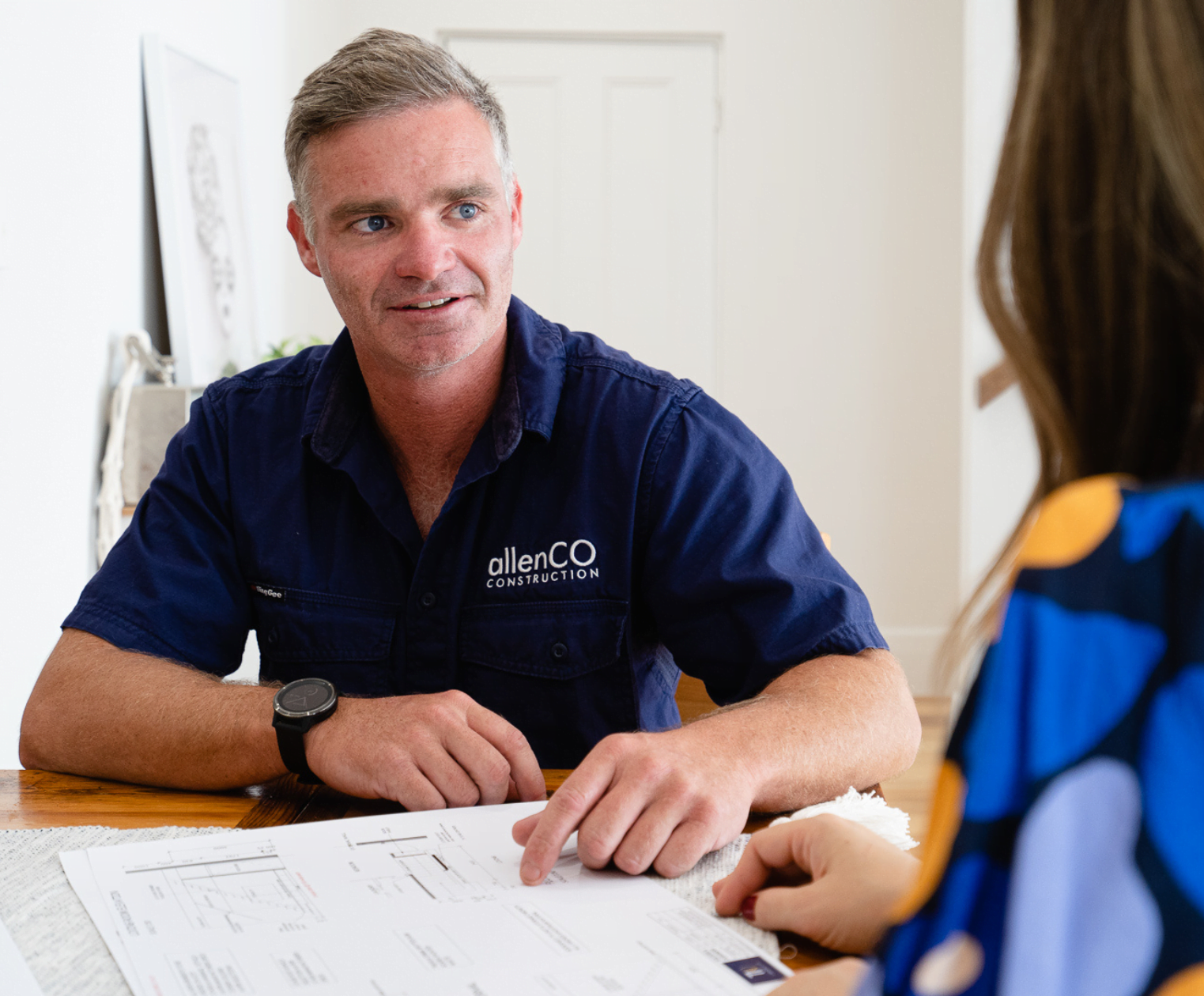 Jade Allen talks to a customer about their building project. He is wearing a dark blue shirt with a small white logo for allenCO Construction.